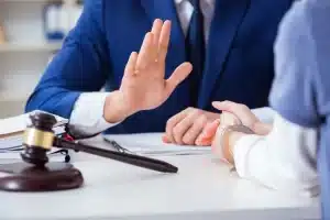 Lawyer holding hand up, with gavel on desk.