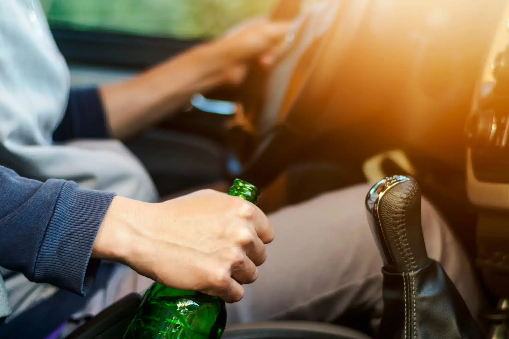 A man holding beer by hip while driving.