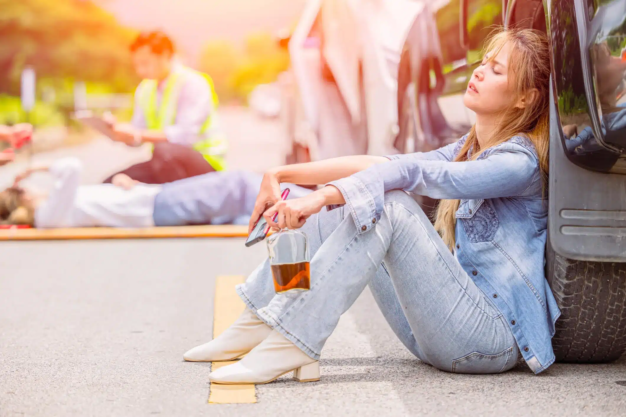 A young woman sitting on ground next to her car after a car accident while driving drunk.