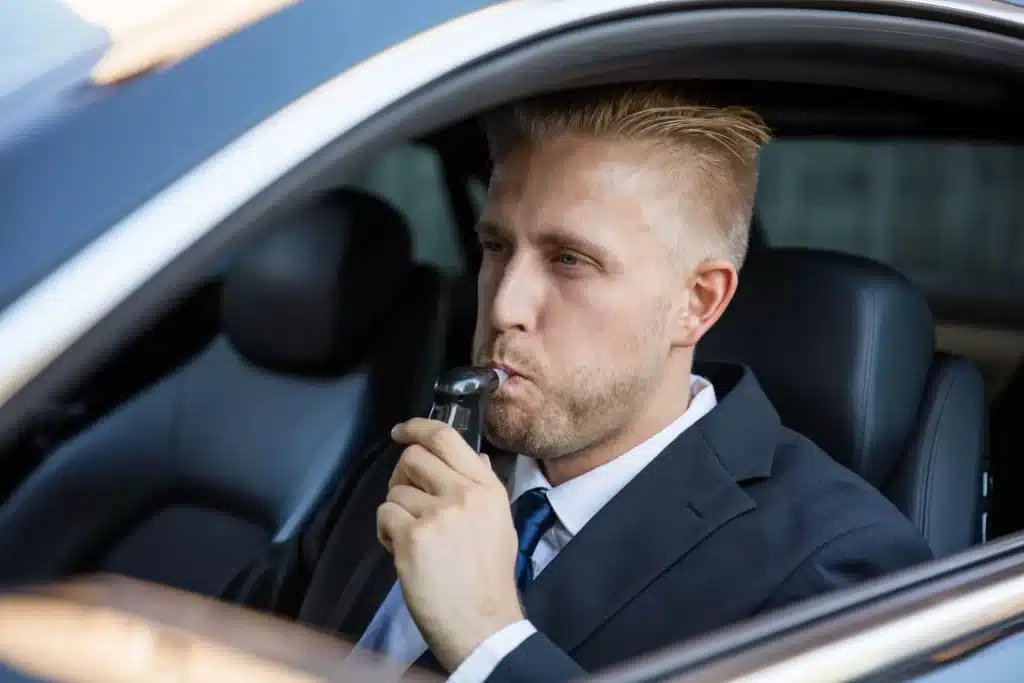A man blowing into a breathalyzer attached to his car.