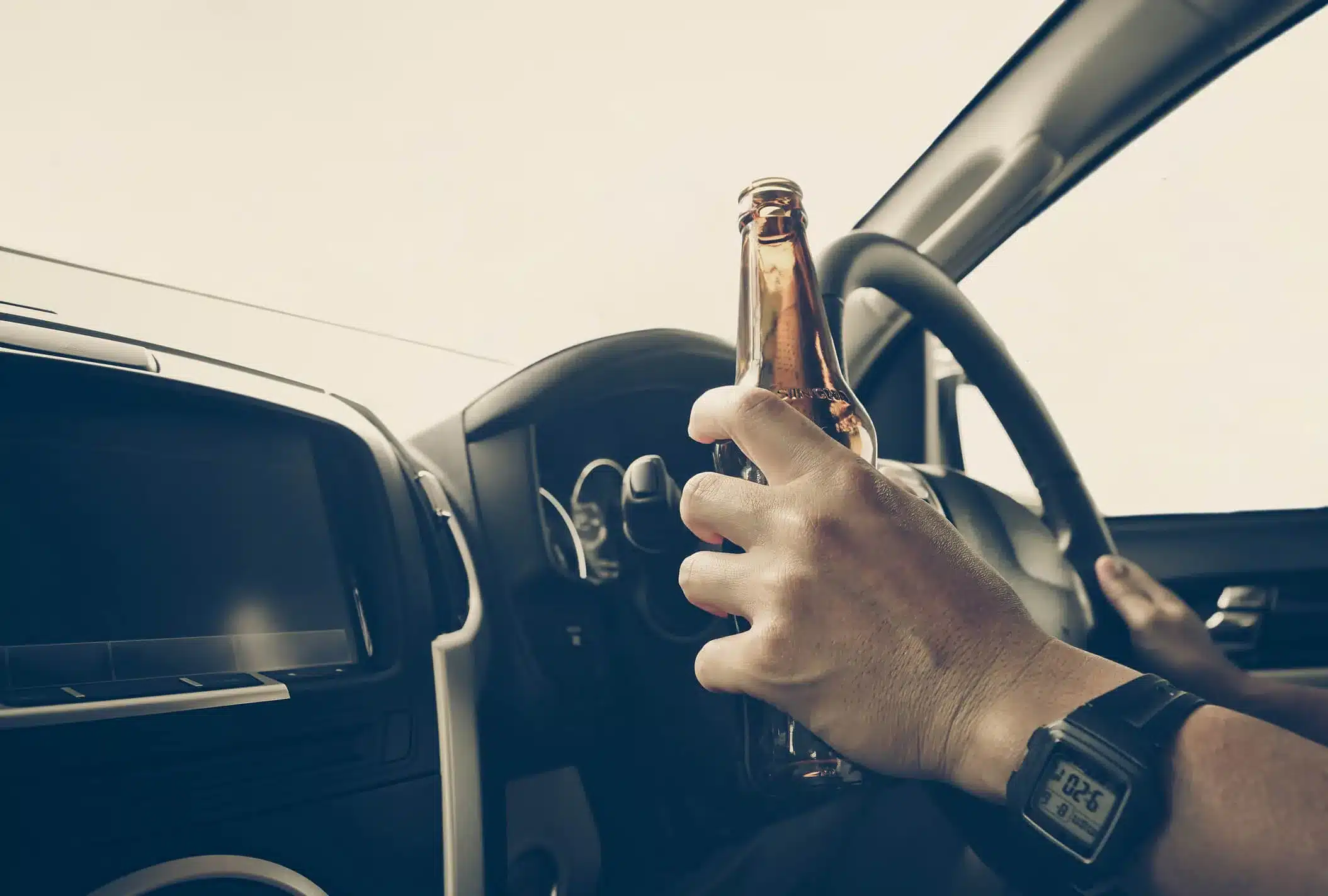 A man drinking a beer while driving his car.