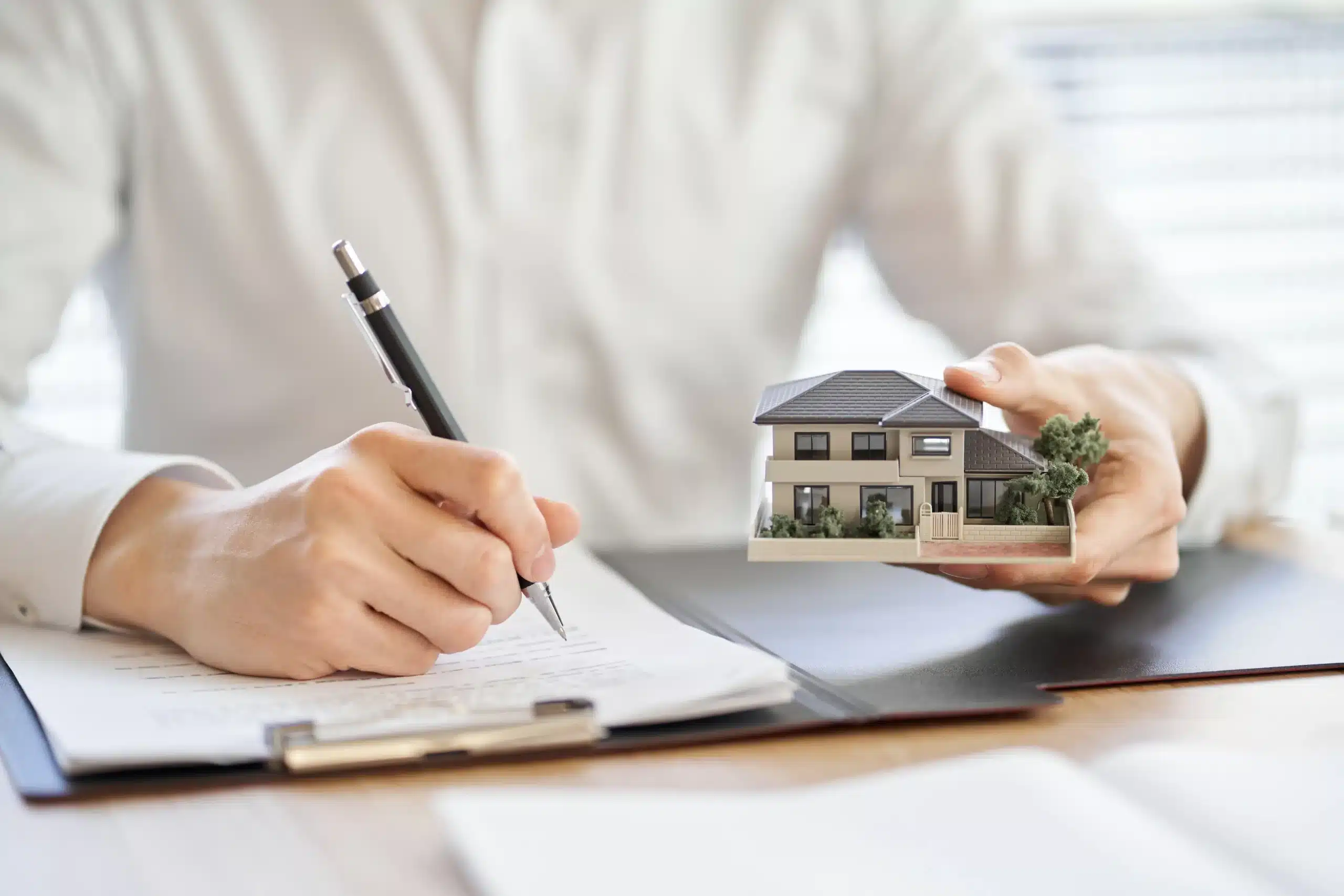 Someone signing house documents and holding a small model of a home.