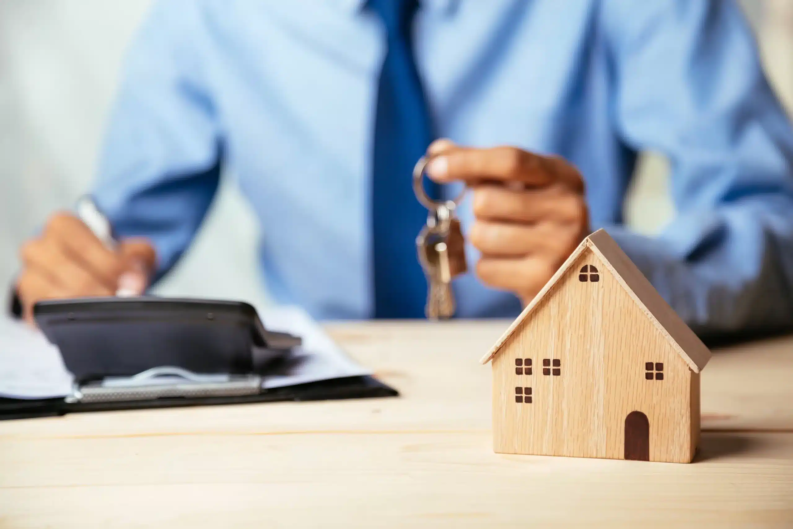 A man holding keys behind a toy house.