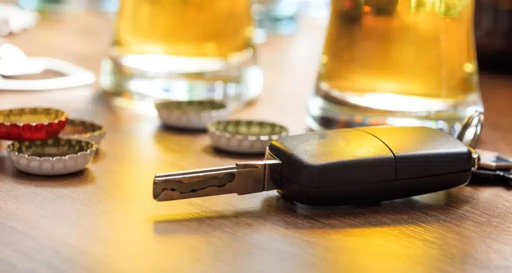 Car keys next to beer caps and glasses of alcohol.