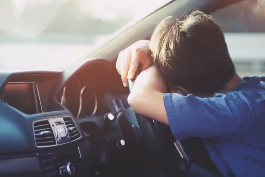 A boy asleep at the wheel in a car.