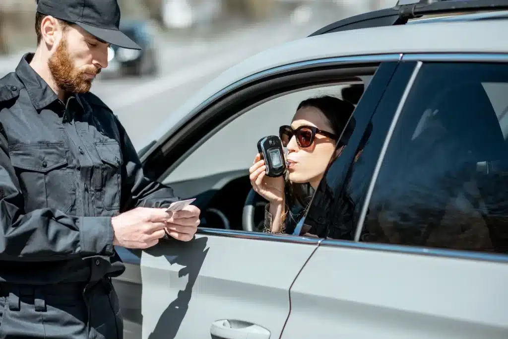 A woman taking a breathalyzer test while the officer is looking at her license.