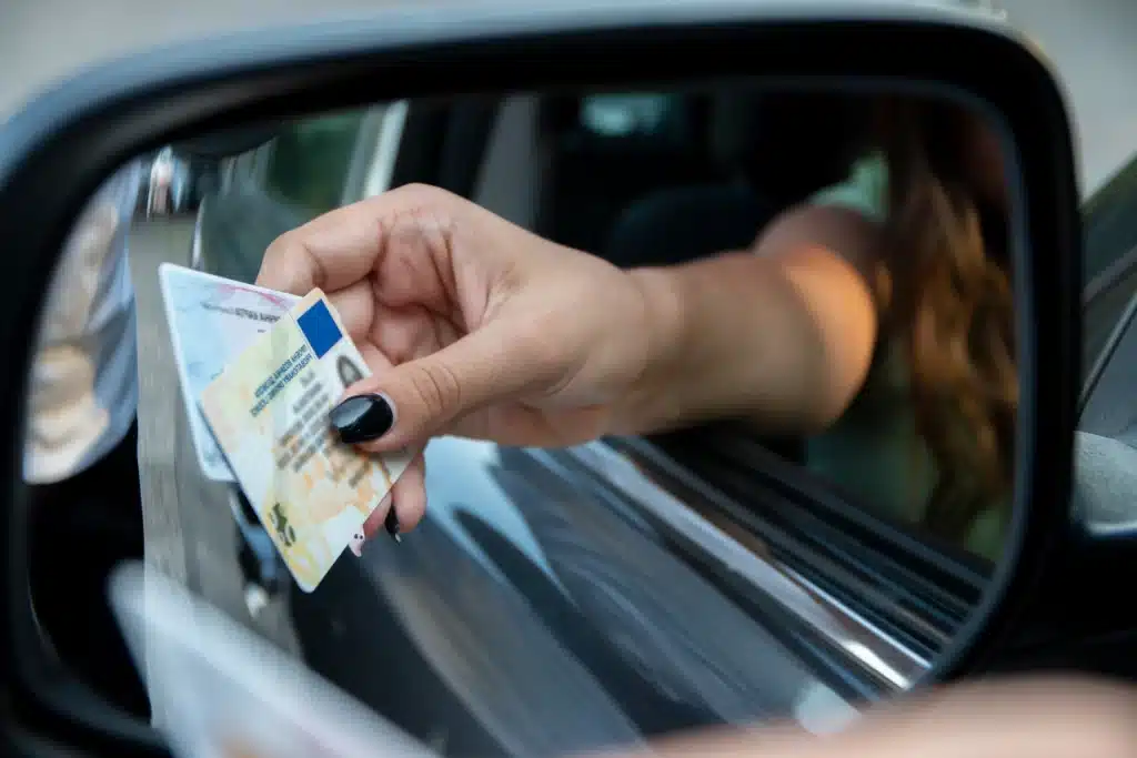 Woman handing her drivers license out of the car window.