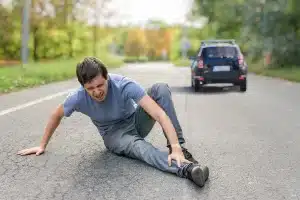 A man sitting in a road who has been hit by a car.